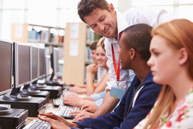 Students Working At Computers In Library With Teacher